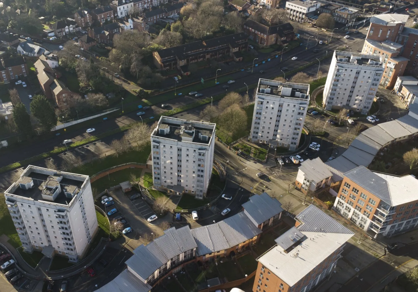 Drone shot of four high rise buildings in the UK surrounded by trees, roads and other residential buildings.