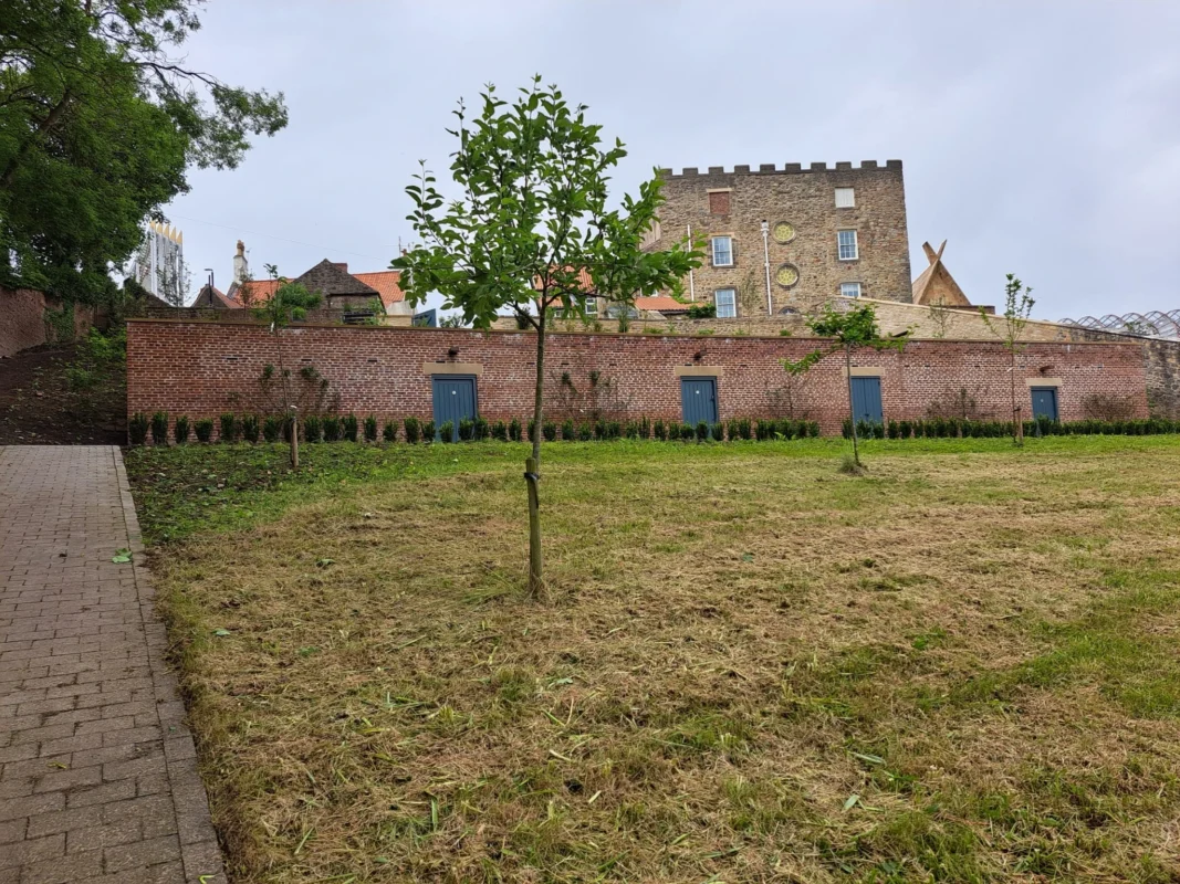 A brick wall and grass in front of Auckland Castle.